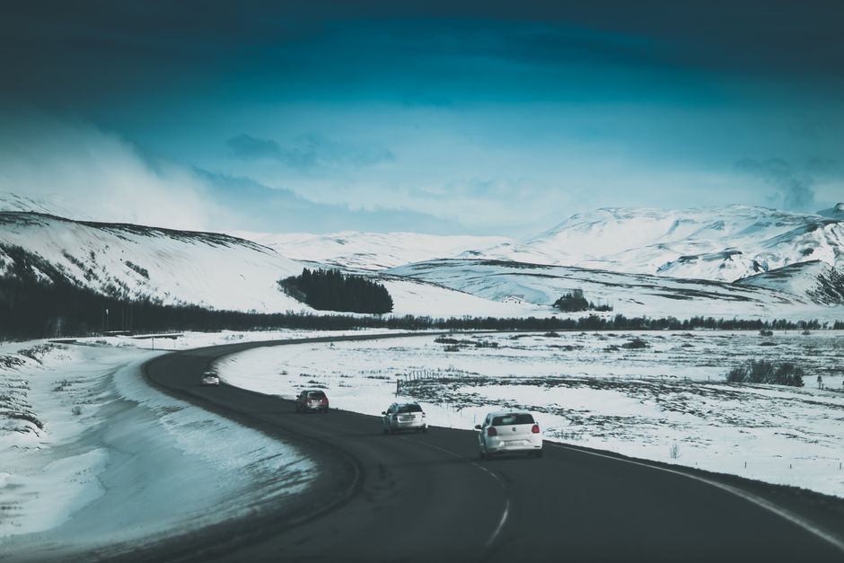 Modern cars driving along curly asphalt road in mountainous terrain covered with snow on winter day