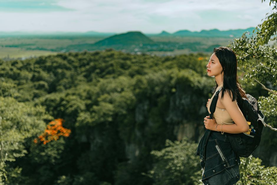 Asian woman enjoying a scenic forest landscape with mountains in the background.