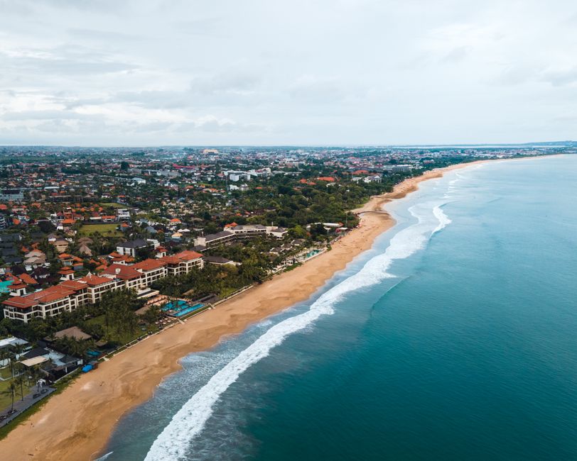 Discover Bali's stunning beachfront with waves and cityscape from above.
