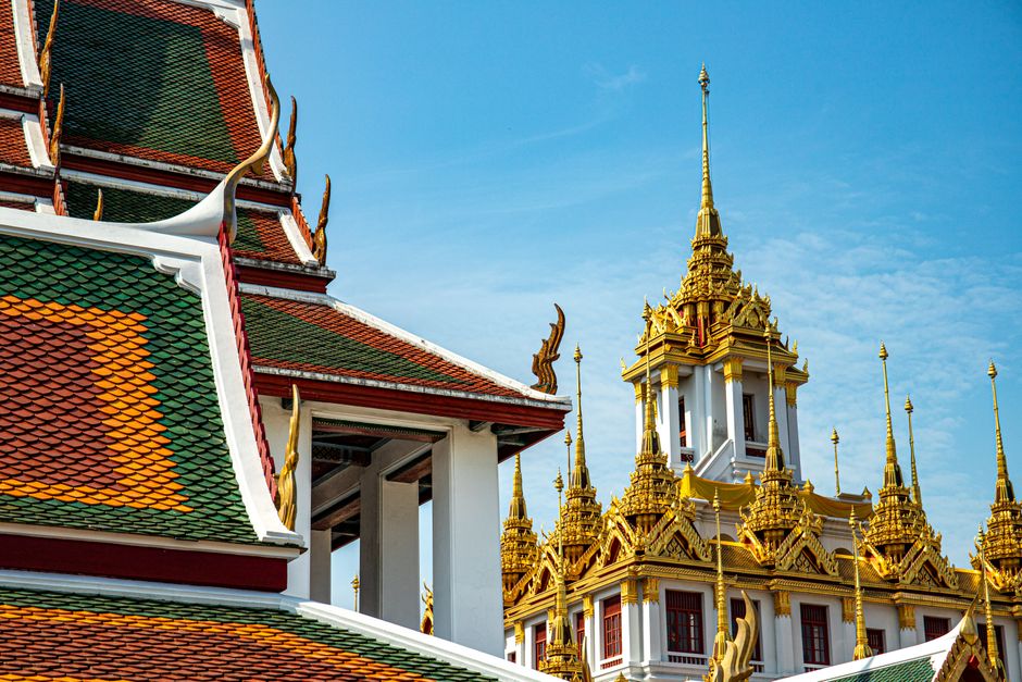 Detailed image of vibrant temple architecture in Bangkok, showcasing golden spires and intricate designs against a clear blue sky.