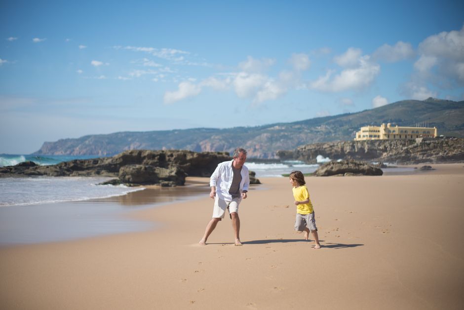 A father and son enjoy a playful moment on a sunny beach in Portugal.