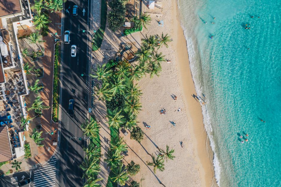 A stunning aerial view of a tropical beach, adjacent road, and vibrant turquoise waters.