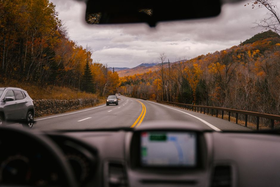 Through windshield of car riding on asphalt roadway between bright yellow trees on cloudy autumn day