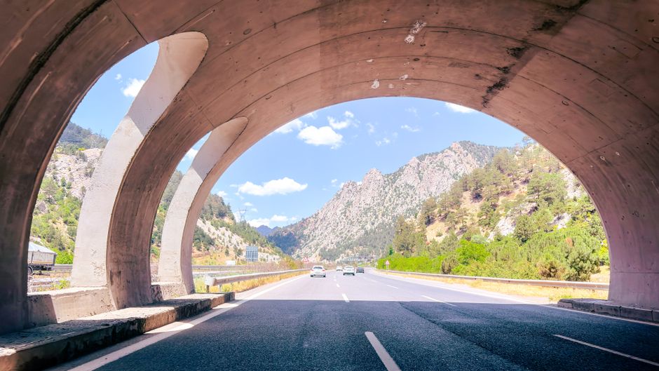 View through a tunnel onto a scenic mountain highway with clear skies.