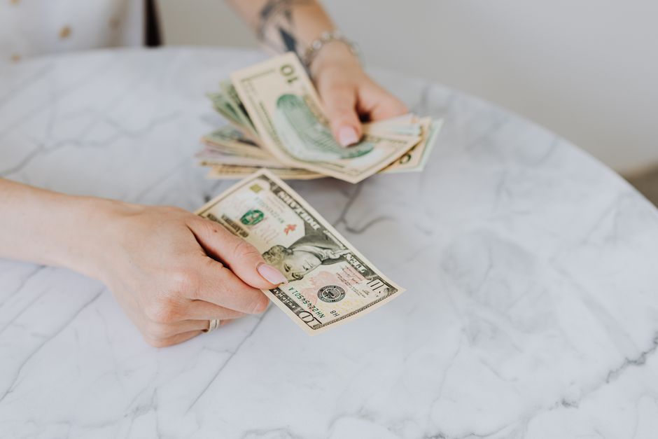 Close-up of hands counting US dollar bills on a marble table surface.