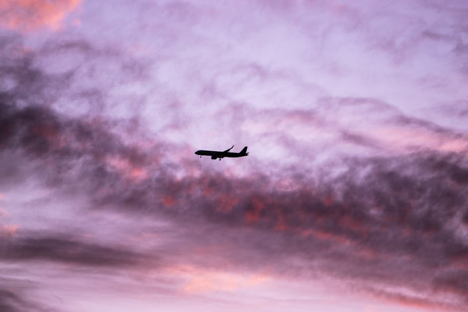 A silhouette of an airplane flying through a vibrant purple and pink sunset sky, capturing a sense of travel and adventure.