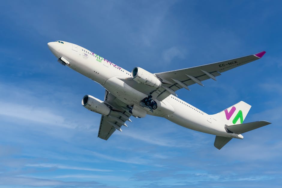Low angle shot of a white airplane flying high, clear blue sky backdrop.