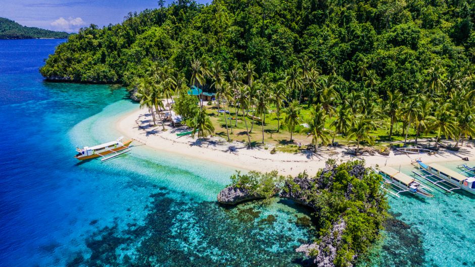 A stunning aerial view of a tropical island beach in the Philippines with turquoise waters and lush greenery.