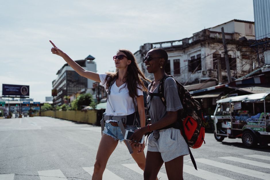 Two women, one pointing forward, explore a vibrant city street, showcasing joy and adventure.