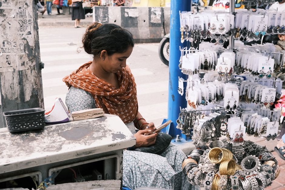 A street vendor sits at her jewelry stall in a bustling Bengaluru market.