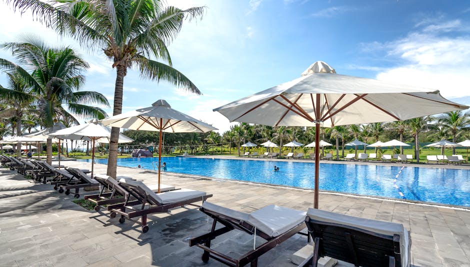 Relaxing tropical resort scene with palm trees, sunbeds, and poolside umbrellas.