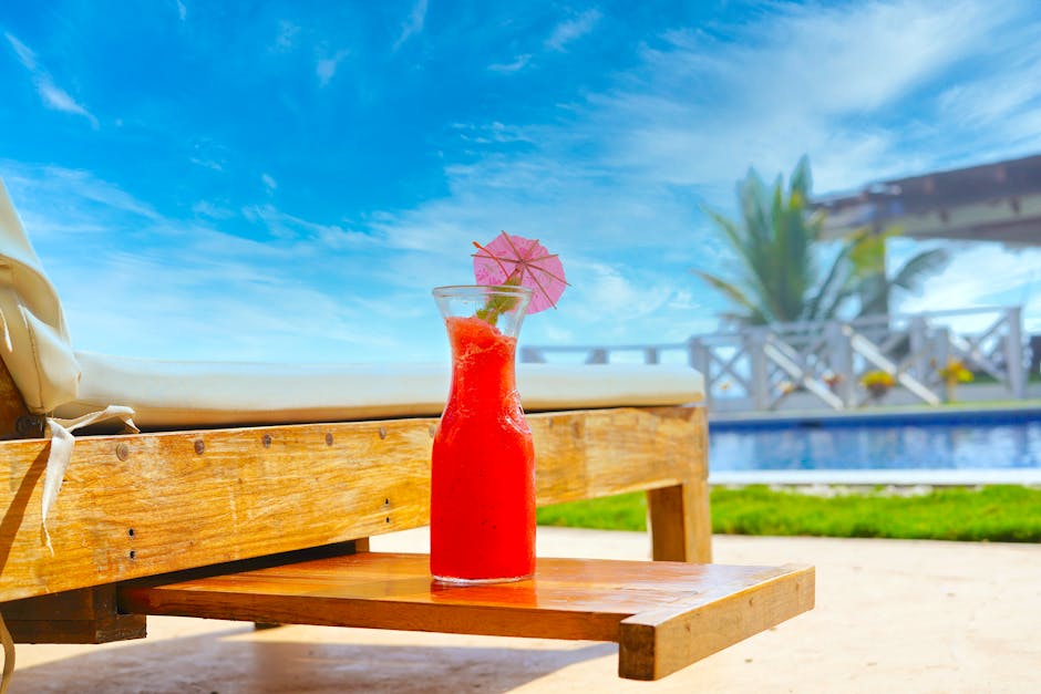 A vibrant red tropical juice with an umbrella by the pool, perfect for a summer day.