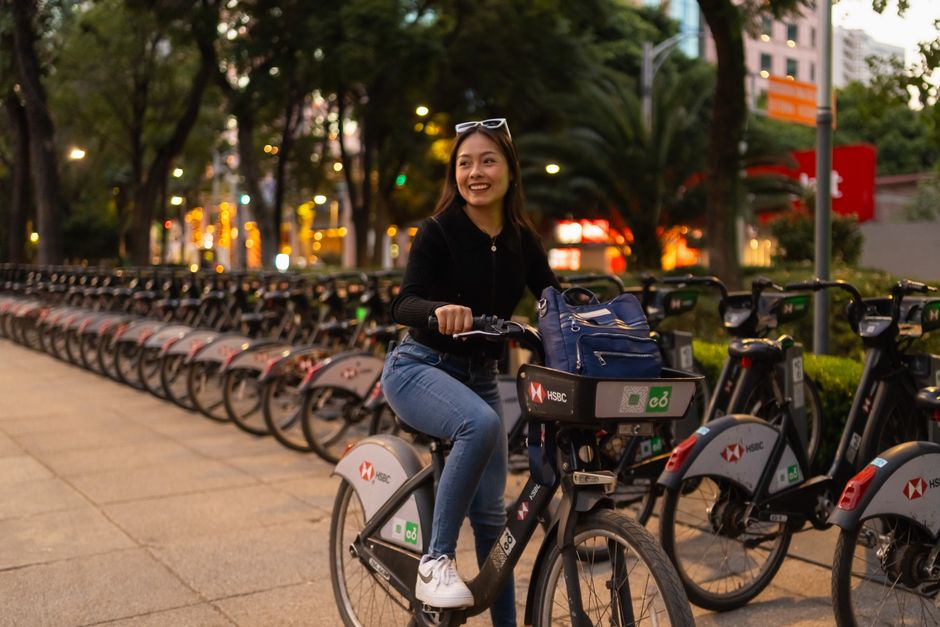 Woman riding a city bike at dusk in Mexico City with a joyful expression.