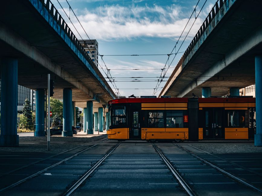 Vibrant yellow tram crossing beneath urban elevated roads on a clear day.