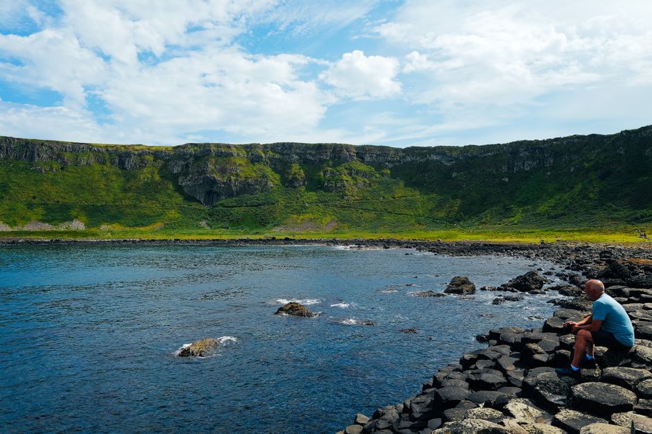 A man sits on the rocky coast of Giant's Causeway, enjoying the scenic view.