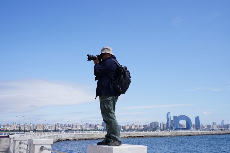 Photographer with camera capturing the cityscape of Baku, Azerbaijan against a clear blue sky.
