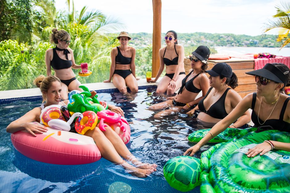 Seven women in bikinis relaxing and having fun at an outdoor pool party.