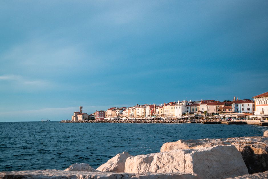 Scenic coastal view of a historic town with vibrant buildings along the shoreline, under a bright sky.