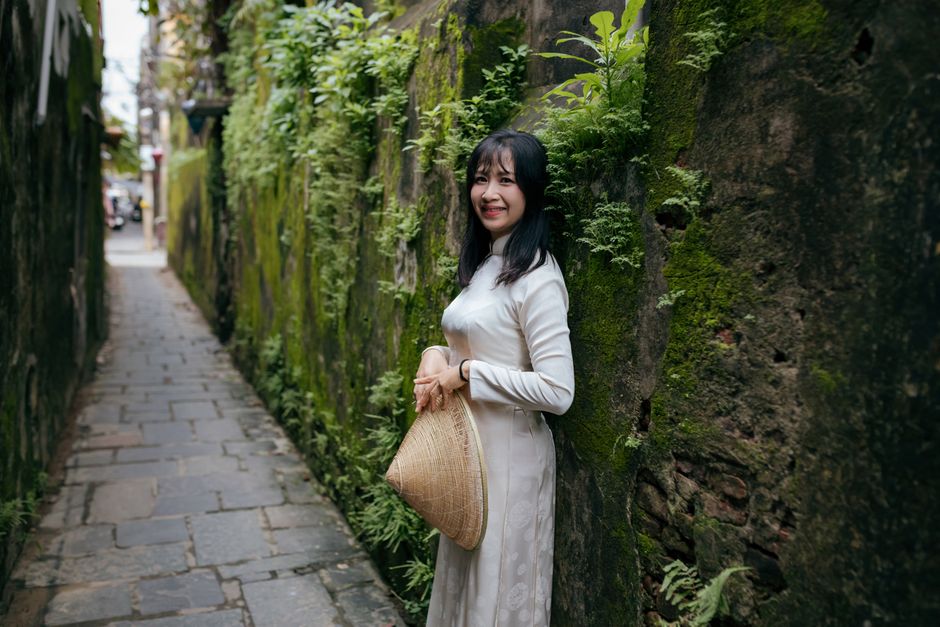 Asian woman in a traditional dress smiles in a lush, narrow alley in Hoi An, Vietnam.