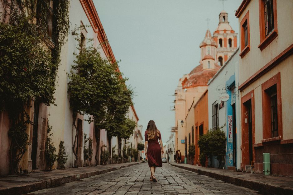 A woman in a maroon dress strolls down a charming cobblestone street lined with colorful buildings and a historic church.
