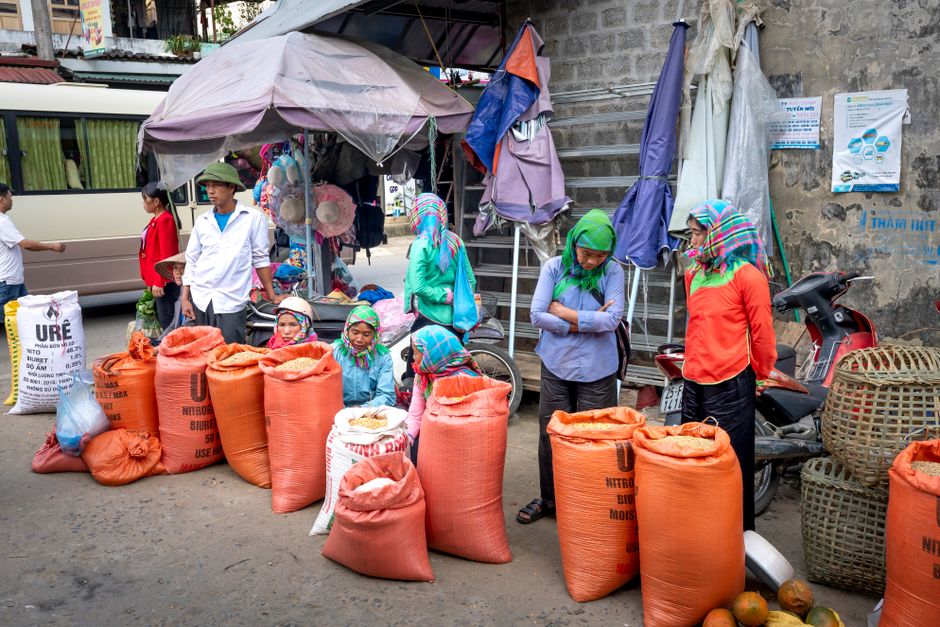 Unrecognizable ethnic sellers with bags of cereals and baskets on pavement in local urban bazaar