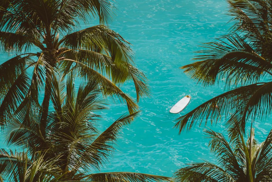 A tranquil view of a surfboard on turquoise water encircled by palm trees.