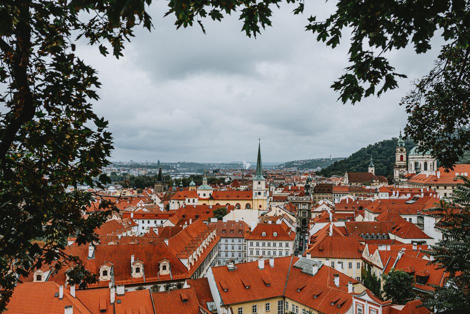 A beautiful aerial view of Prague's iconic red rooftops framed by trees on a cloudy day.
