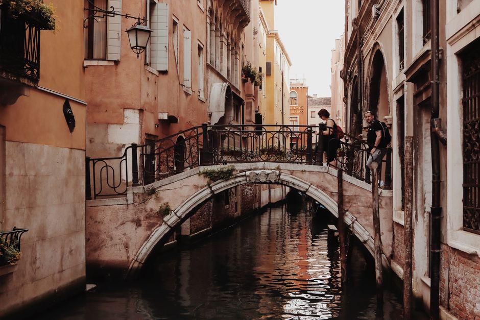 Classic view of Venice's canals featuring a footbridge and historic architecture, with tourists exploring.