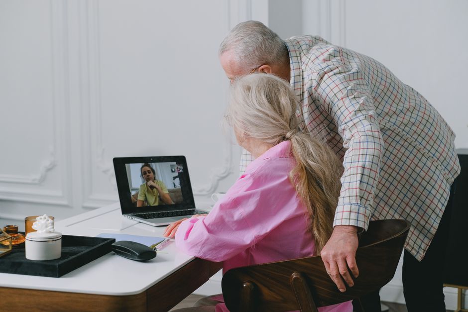 Elderly couple using laptop for a video call in a cozy indoor setting.