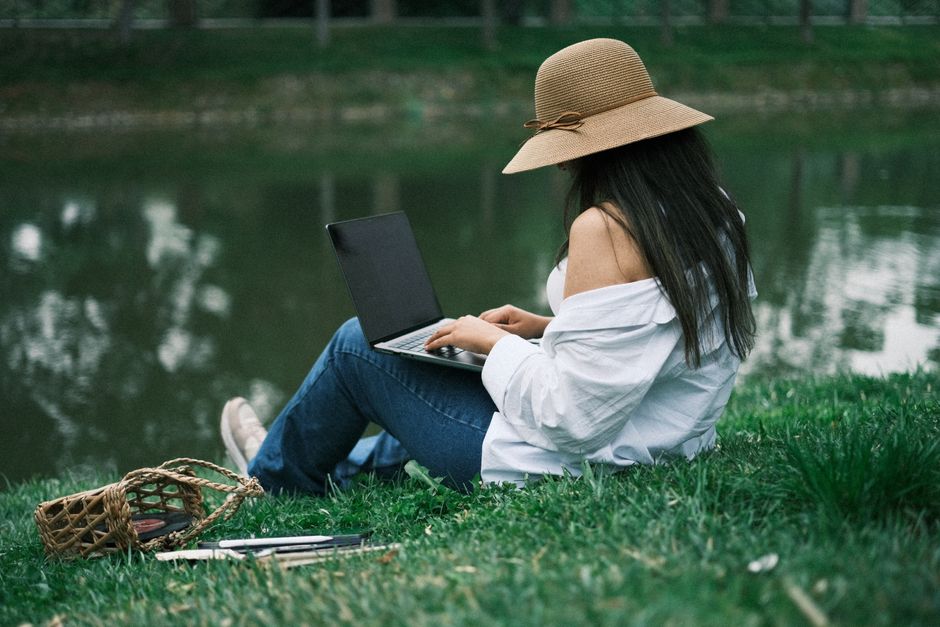 Young woman using laptop in a park by a lake, embracing remote work in nature.