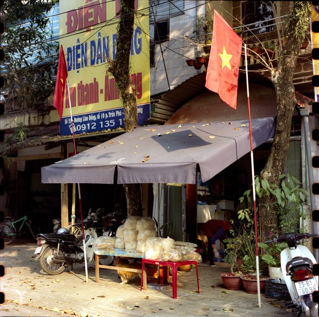 Vietnamese street with motor scooters, flags, and a small storefront.
