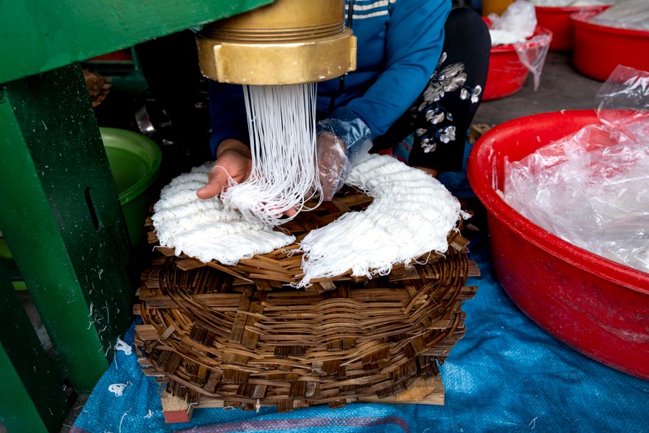 Crop faceless person in casual clothes sitting and making noodle with metal machine near basins on manufacture in Vietnam