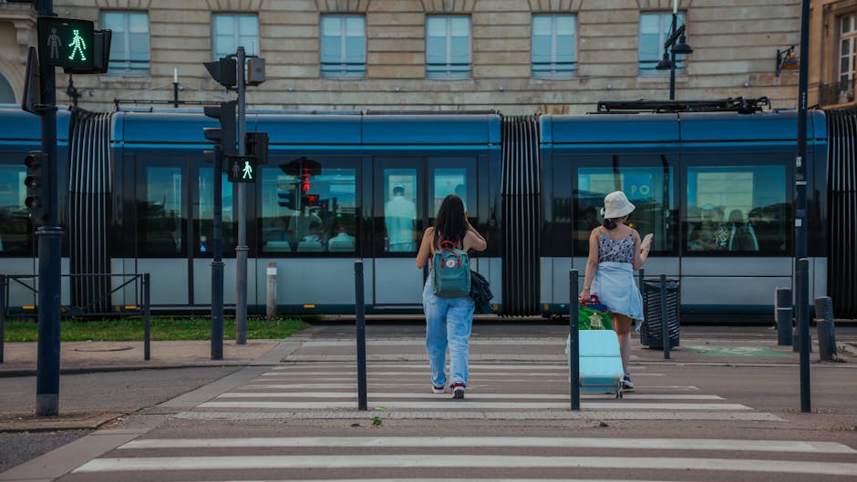 Two women cross a street in front of a tram in Bordeaux, France on a sunny day.