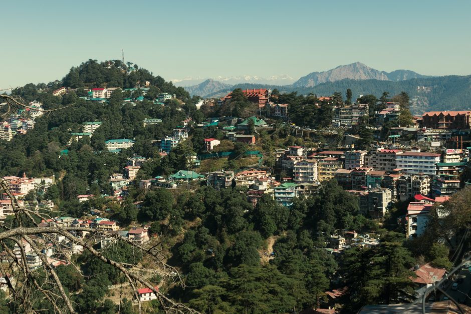 A picturesque view of a hill town surrounded by lush greenery and majestic mountains in the background.